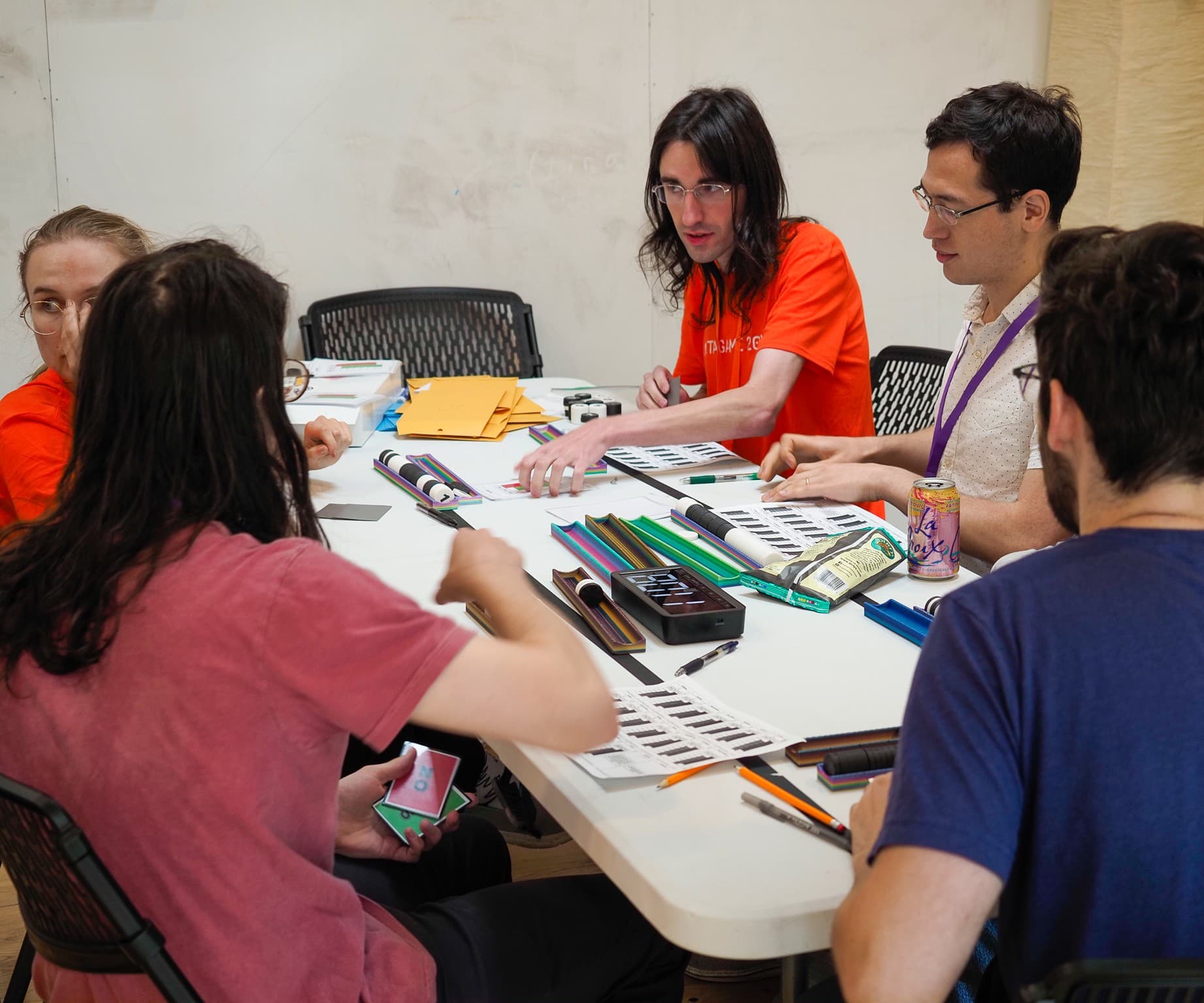 Players gathered around a table mid-game at Metagame 2025, cards and scoring strips spread between them